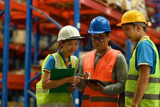 Senior male manager and warehouse workers are inspecting stock tick and cardboard stock product on digital tablet in a large warehouse.