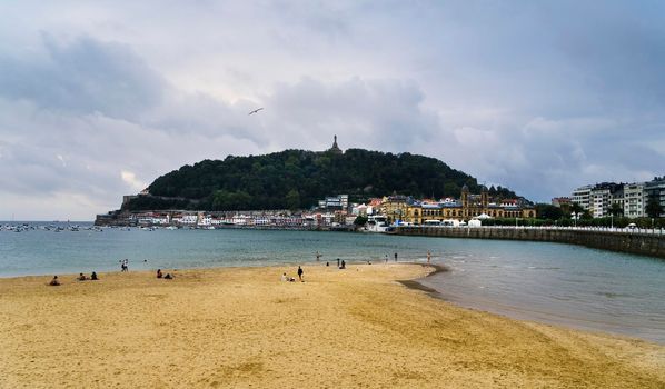 Landscape of La Concha beach in the city of San Sebastian, on a sunny day with people enjoying the beach and Mount Urgull in the background.