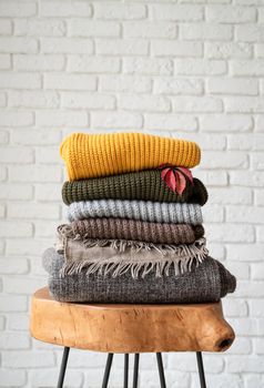 Hello fall. Cozy warm image. Stack of autumn warm sweaters on modern coffee table, white brick wall background