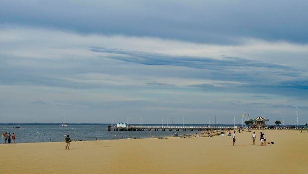 Landscape of the beach in the French town of Arcachon with tourists and the harbour in the background.