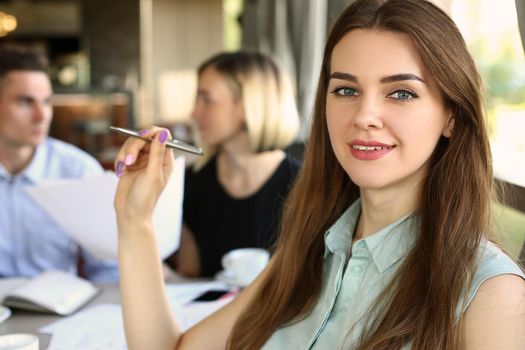 Portrait of a beautiful business woman sitting in cafe with colleagues discussing business project in background. Business meeting and discussion of business development