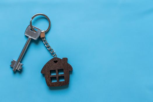 Key with a house keychain on a colored blue background. Real estate agent. Buying a house, apartment
