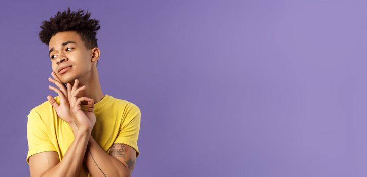 Close-up portrait of glamour beautiful young queer guy with dreads, standing in feminine model pose, gently touching face and looking away sensual, standing purple background.