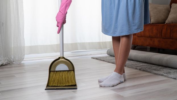 A woman in pink gloves cleans the apartment with a scoop and a broom close-up of her legs