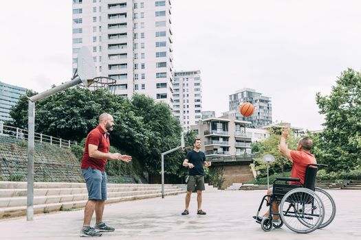 joyful disabled man in wheelchair playing with a basket ball with friends, concept of adaptive sports and physical activity, rehabilitation for people with physical disabilities