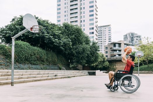 handicapped man in wheelchair throwing ball to basket alone, concept of adaptive sports and physical activity, rehabilitation for people with physical disabilities