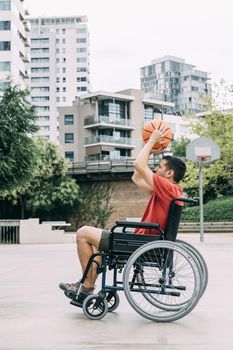 handicapped man in wheelchair playing basketball alone in the city, concept of adaptive sports and physical activity, rehabilitation for people with physical disabilities, vertical photo
