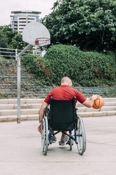 disabled man in wheelchair playing basketball alone in the city, concept of adaptive sports and physical activity, rehabilitation for people with physical disabilities, vertical photo