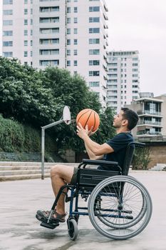 disabled man in wheelchair playing basketball alone, concept of adaptive sports and physical activity, rehabilitation for people with physical disabilities, vertical photo