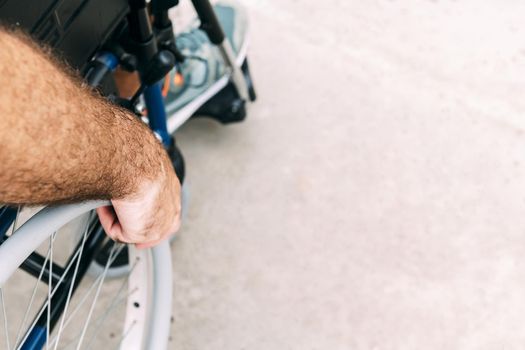 Close up of disabled man sitting in a wheelchair, he holds his hand on the wheel
