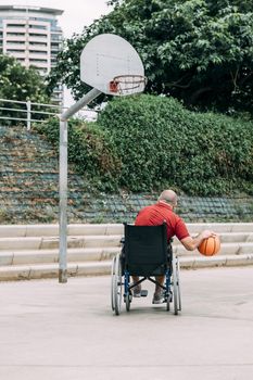 man in wheelchair playing basketball alone in the city, concept of adaptive sports and physical activity, rehabilitation for people with physical disabilities, vertical photo