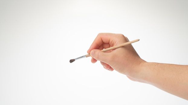 Drawing brush in a man's right hand, gesture to draw. High quality photo