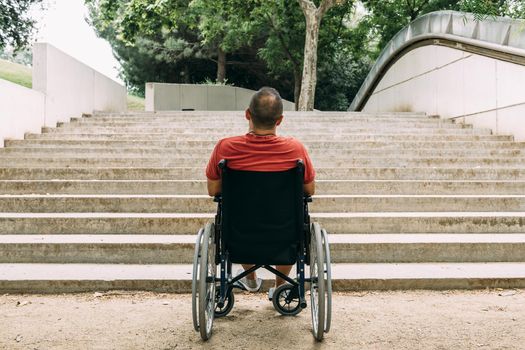 disabled man on wheelchair stopped in front of stairs who can't climb looking up for help, raising awareness of accessibility issues for people with reduced mobility