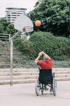 handicapped man in wheelchair playing basketball alone in the city, concept of adaptive sports and physical activity, rehabilitation for people with physical disabilities, vertical photo