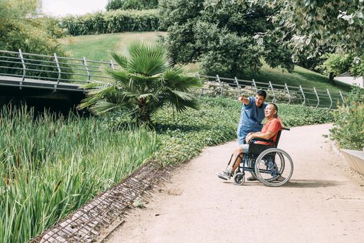 caretaker talking with his disabled patient in a wheelchair during a walk, concept of medical care and rehabilitation of people with disabilities and reduced mobility problems