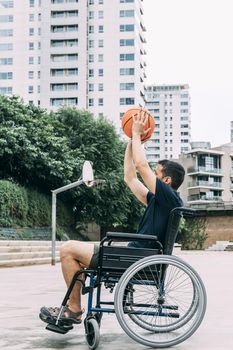 disabled man in wheelchair throwing ball to basket alone, concept of adaptive sports and physical activity, rehabilitation for people with physical disabilities, vertical photo