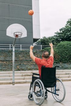 disabled man in wheelchair playing basketball alone in the city, concept of adaptive sports and physical activity, rehabilitation for people with physical disabilities, vertical photo