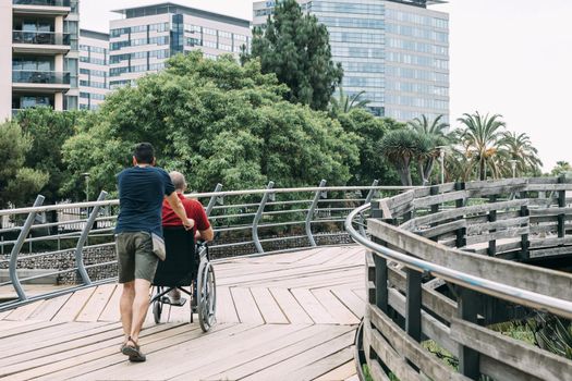 man pushes his disabled friend's wheelchair into the park, concept of friendship and integration of people with disabilities and reduced mobility problems