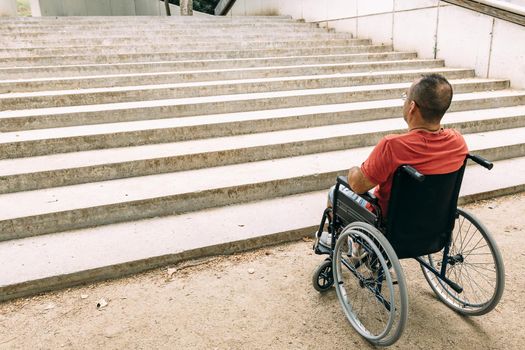 disabled person on wheelchair stopped in front of stairs who can't climb looking up for help, raising awareness of architectural barriers and accessibility issues for people with reduced mobility