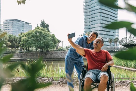 disabled man in a wheelchair taking a picture with his caretaker during a walk, concept of medical care and rehabilitation of people with disabilities and reduced mobility problems