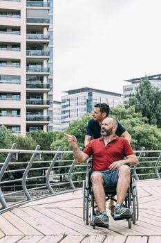 disabled man in wheelchair conversing with his friend during a walk, concept of friendship and integration of people with disabilities and reduced mobility problems, vertical photo