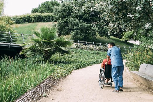 man pushes his disabled patient's wheelchair into the park, concept of medical care and rehabilitation of people with disabilities and reduced mobility problems