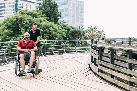 disabled man in wheelchair walks with a friend in the park, concept of friendship and integration of people with disabilities and reduced mobility problems