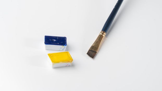 Blue and yellow watercolor paints in separate ditches with a brush for drawing on a white background. High quality photo