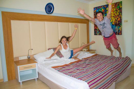 A man and a woman have fun - jumping on the bed in the hotel, a funny couple. High quality photo