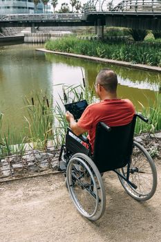 disabled man in wheelchair having fun while working using a tablet computer at park, concept of technological and occupational integration of people with disabilities and reduced mobility problems