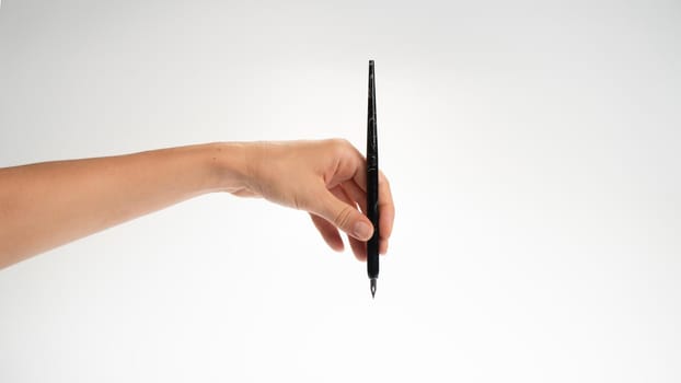 Female left hand holds a calligraphy pen on a white background, gesture drops into the inkwell. High quality photo