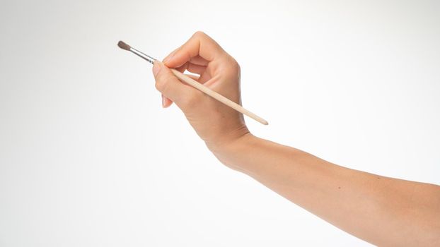 Drawing brush in a woman's right hand, gesture to draw on a white background. High quality photo
