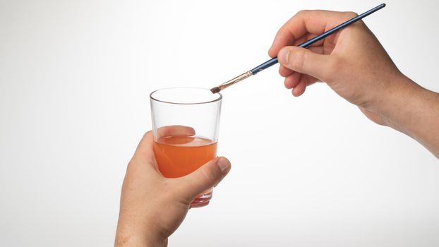 men's hand cleans the brush from the paint in a glass of water