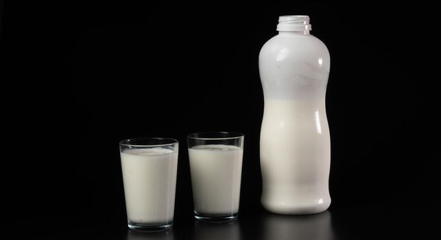 Glass with milk or kefir on a black background with a white bottle. High quality photo