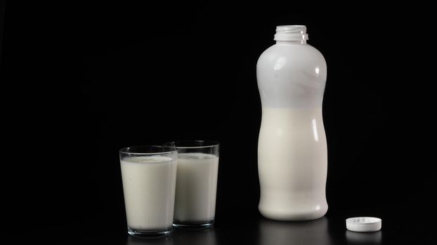 A bottle of kefir or milk with two filled glasses on a black background. High quality photo