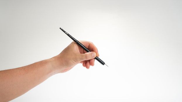 A man's hand holds a calligraphy and writing pen in his left hand on a white background. High quality photo