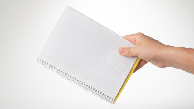 A man's hand holds a notebook in a cage on a white background. High quality photo