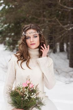 Beautiful bride in a white dress with a bouquet in a snow-covered winter forest. Portrait of the bride in nature.