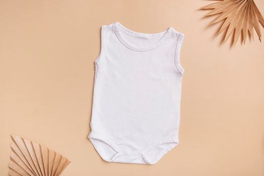 White baby bodysuit mock-up for logo, text or design on beige background with palm leaves top view