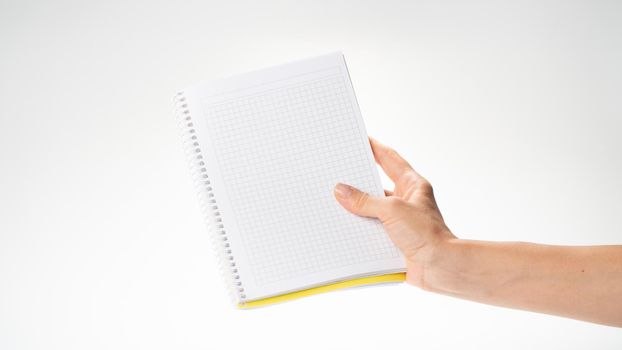 A woman's right hand holds a notebook in a cage on a white background space for inscription. High quality photo