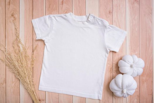 White baby t-shirt top view. Mock-up for logo, text or design on wooden background. Flat lay child clothes with pumpkins.