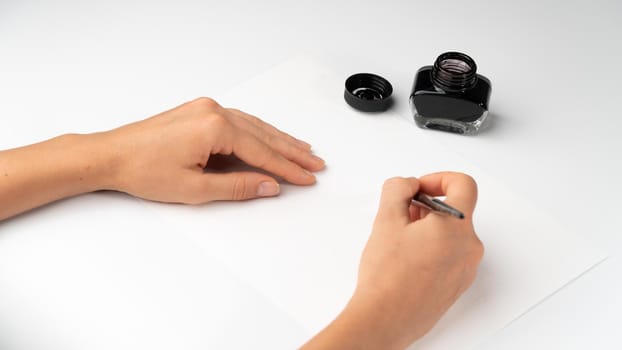 A woman's hands hold a fountain pen on a white background with calligraphy ink