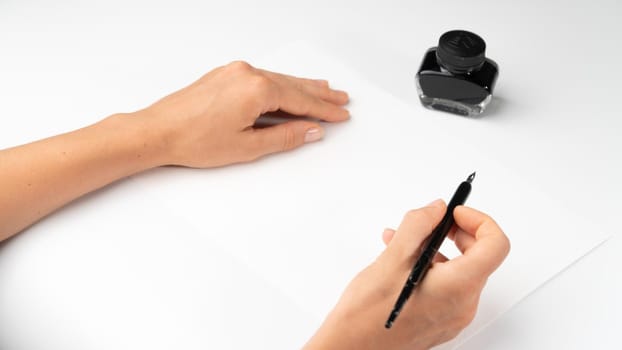 A woman's hands hold a fountain pen on a white background with calligraphy ink