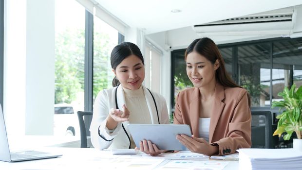 Two beautiful young asian businesswoman working together using digital tablet at office..