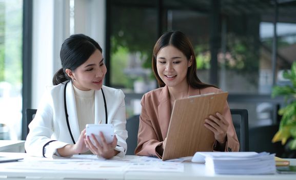 Two young Asian businesswoman discuss investment project working and planning strategy. Business people talking together with laptop computer at office..