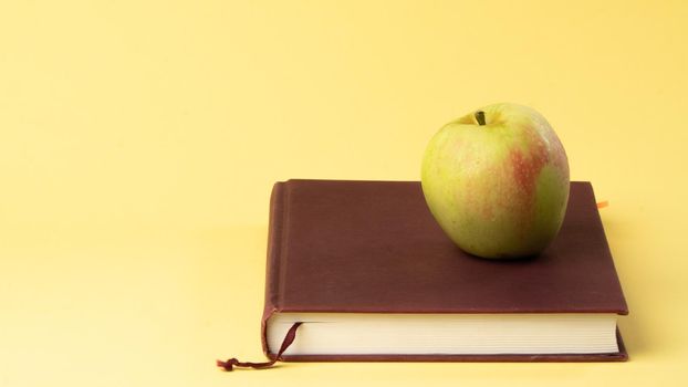 Book and apple on the table on a yellow background, study, autumn. High quality photo
