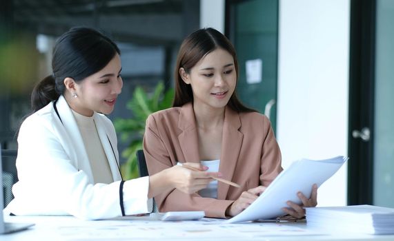 Two young Asian businesswoman discuss investment project working and planning strategy. Business people talking together with laptop computer at office..