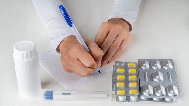 The doctor makes a note on the table with pills and a thermometer. High quality photo