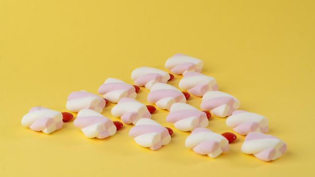 Marshmallows and red candy dragees in the form of a triangle on a yellow background. High quality photo
