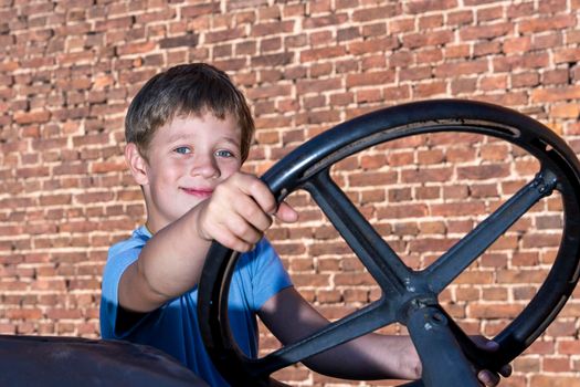 Caucasian preschool boy having fun in the summer on an old tractor outdoors, pretending to drive an old tractor. close-up. portrait
